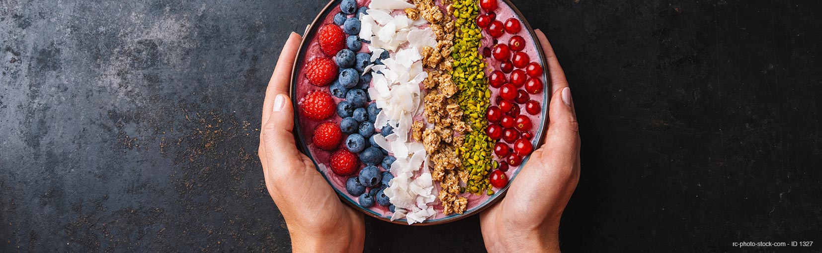 Woman hands hold a Healthy breakfast bowl, wirh blueberry smoothie with, raspberry, blueberrys, coconut, nuts and currants toppings from ©rcfotostock